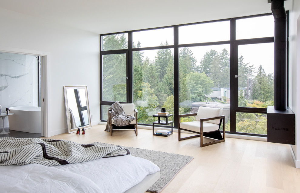 Großes Modernes Hauptschlafzimmer mit weißer Wandfarbe, hellem Holzboden, Hängekamin, Kaminumrandung aus Metall und beigem Boden in Vancouver