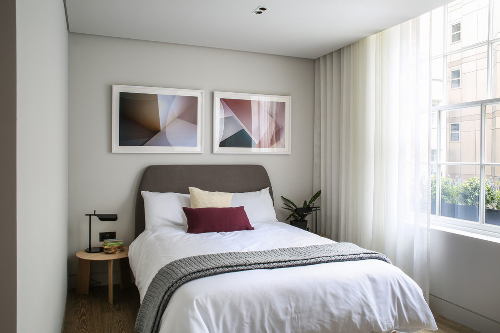 Photo of a small contemporary guest bedroom in London with white walls, light hardwood flooring and no fireplace.