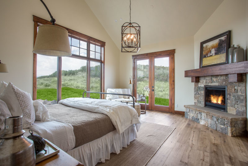 Example of a large mountain style master light wood floor bedroom design in Salt Lake City with beige walls, a standard fireplace and a stone fireplace