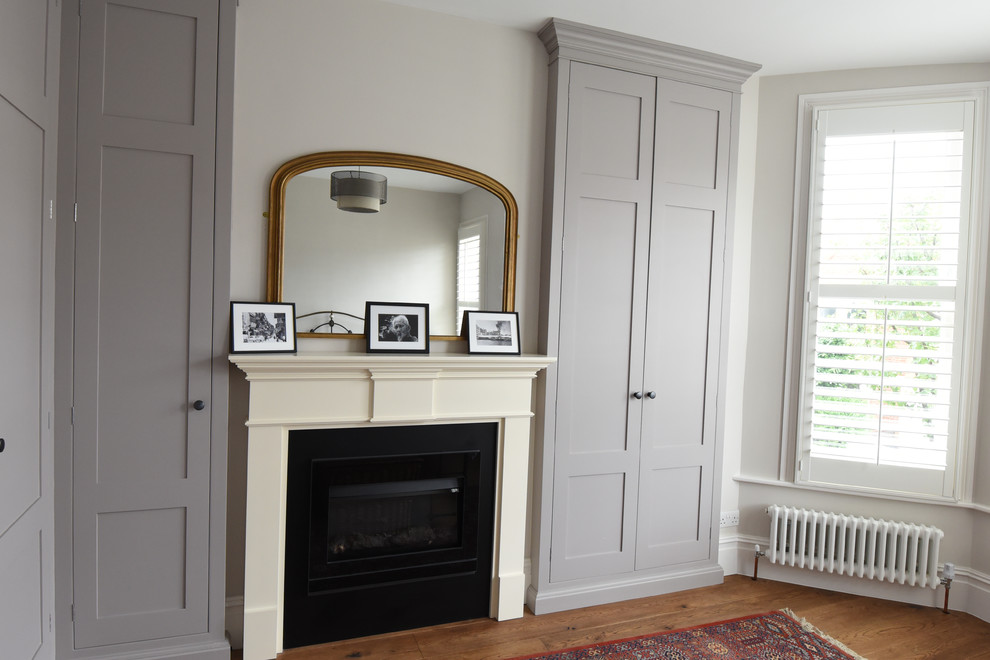 Inspiration pour une grande chambre parentale minimaliste avec un mur beige, parquet foncé, une cheminée standard et un manteau de cheminée en pierre.