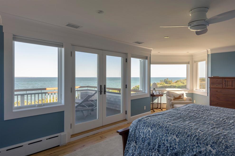 Modelo de dormitorio principal costero de tamaño medio sin chimenea con paredes azules, suelo de madera en tonos medios y suelo marrón