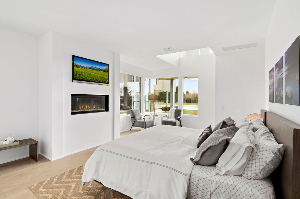Ejemplo de dormitorio principal contemporáneo grande con paredes blancas, suelo de madera clara, chimenea lineal y suelo marrón