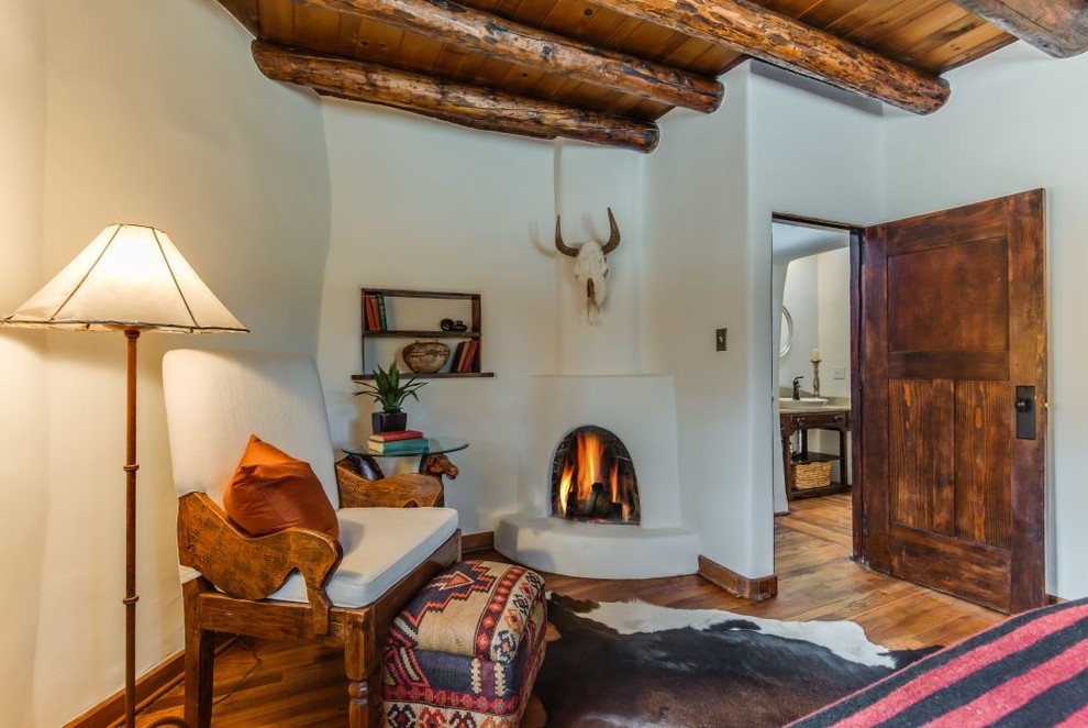 アルバカーキにある中くらいなサンタフェスタイルのおしゃれな主寝室 (ベージュの壁、無垢フローリング、漆喰の暖炉まわり、コーナー設置型暖炉、茶色い床) のレイアウト