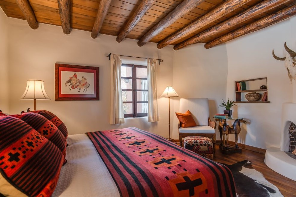 Mittelgroßes Mediterranes Hauptschlafzimmer mit beiger Wandfarbe, braunem Holzboden, verputzter Kaminumrandung und Eckkamin in Albuquerque