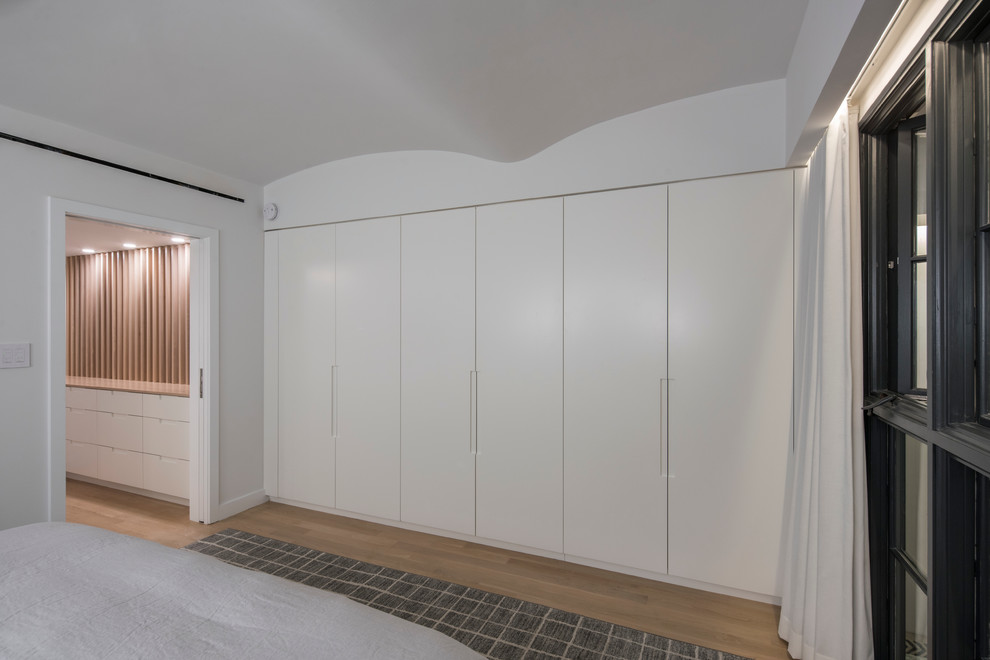 Großes Modernes Hauptschlafzimmer ohne Kamin mit weißer Wandfarbe, hellem Holzboden und braunem Boden in New York