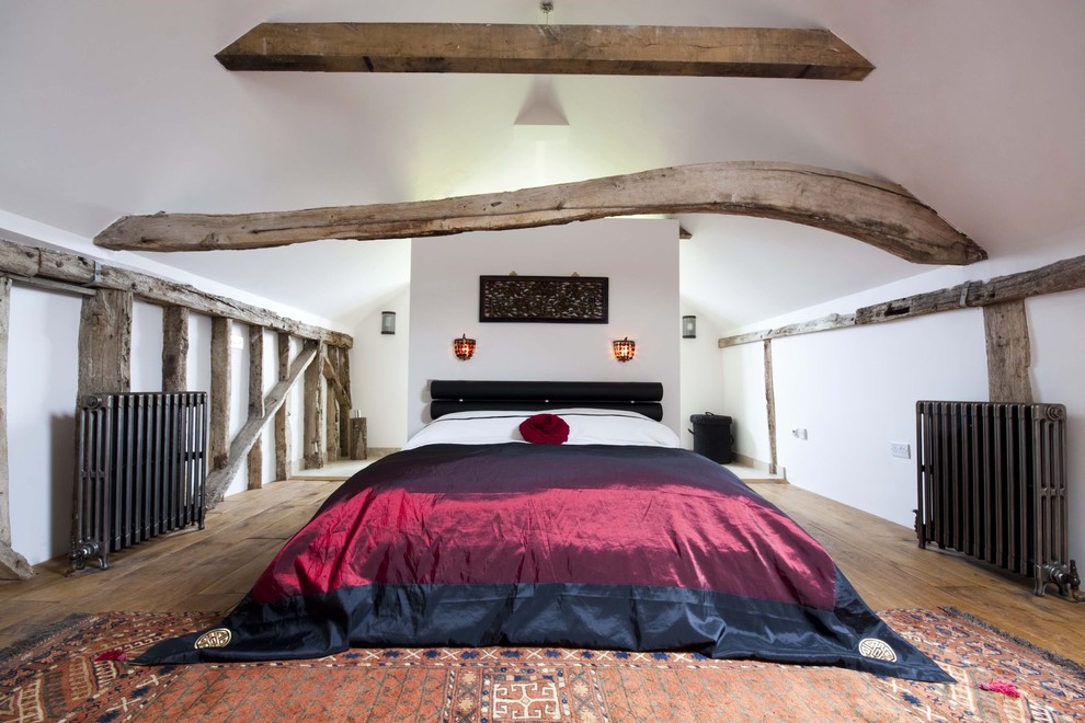 This is an example of a country loft bedroom in London with white walls and medium hardwood flooring.