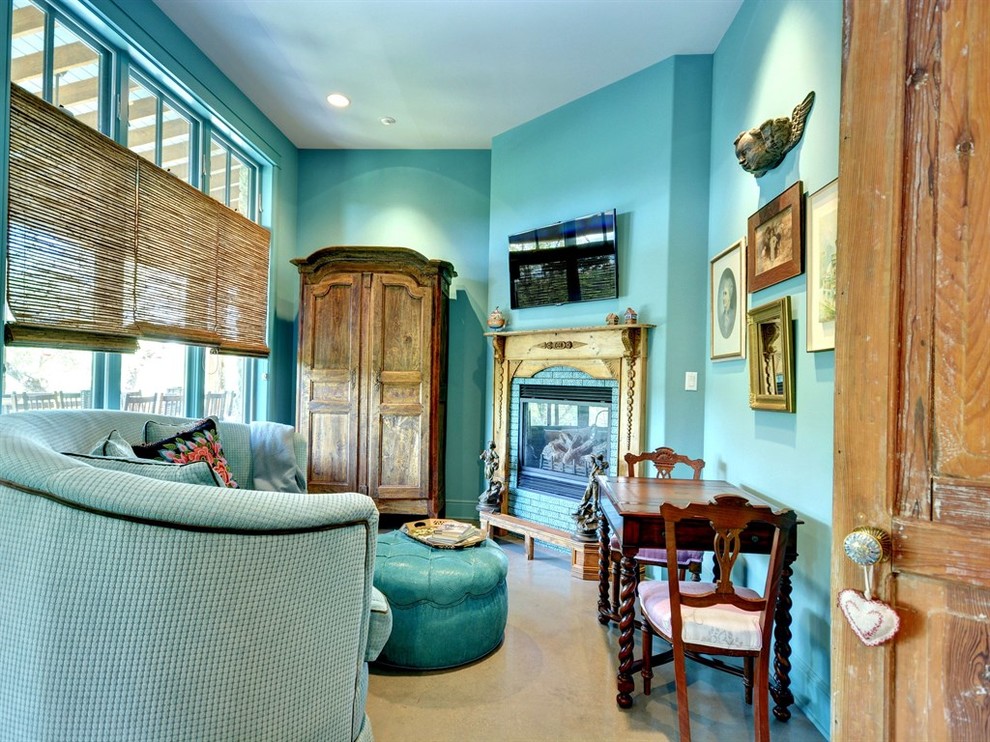 オースティンにある中くらいなエクレクティックスタイルのおしゃれな主寝室 (青い壁、コンクリートの床、コーナー設置型暖炉、レンガの暖炉まわり、グレーの床) のインテリア