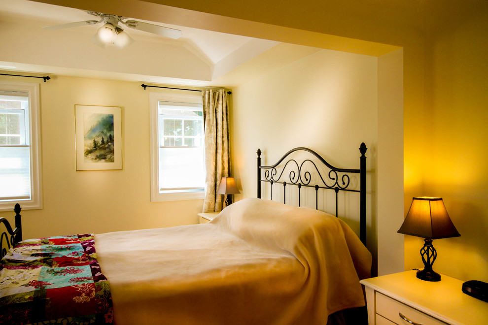Diseño de dormitorio principal clásico renovado de tamaño medio con paredes amarillas y suelo de madera clara