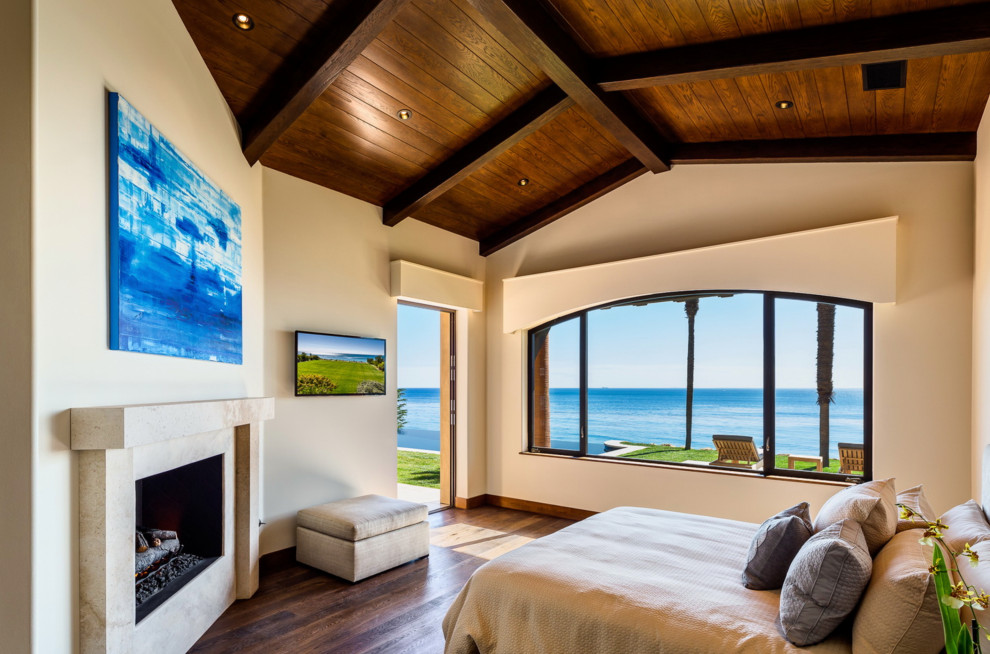 マイアミにある広い地中海スタイルのおしゃれな客用寝室 (ベージュの壁、無垢フローリング、標準型暖炉、タイルの暖炉まわり、茶色い床) のインテリア