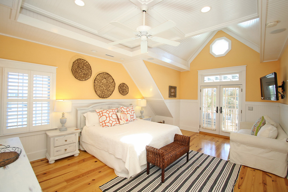 Ejemplo de dormitorio principal costero grande sin chimenea con paredes amarillas, suelo de madera en tonos medios y suelo marrón