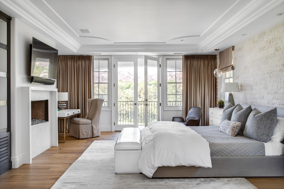 ロサンゼルスにある広い地中海スタイルのおしゃれな主寝室 (白い壁、無垢フローリング、標準型暖炉、タイルの暖炉まわり、ベージュの床、グレーとブラウン)