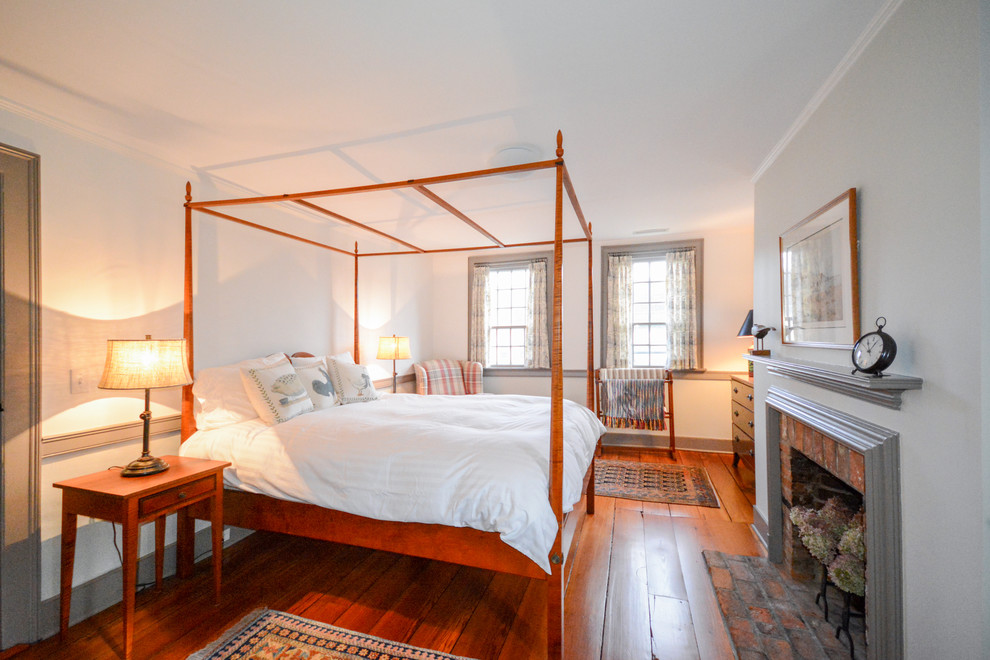 Diseño de dormitorio principal clásico de tamaño medio con paredes blancas, suelo de madera en tonos medios, todas las chimeneas y marco de chimenea de ladrillo