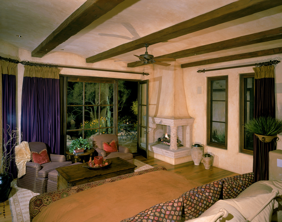 Cette image montre une très grande chambre parentale sud-ouest américain avec un mur beige, un sol en carrelage de céramique, une cheminée d'angle et un manteau de cheminée en pierre.