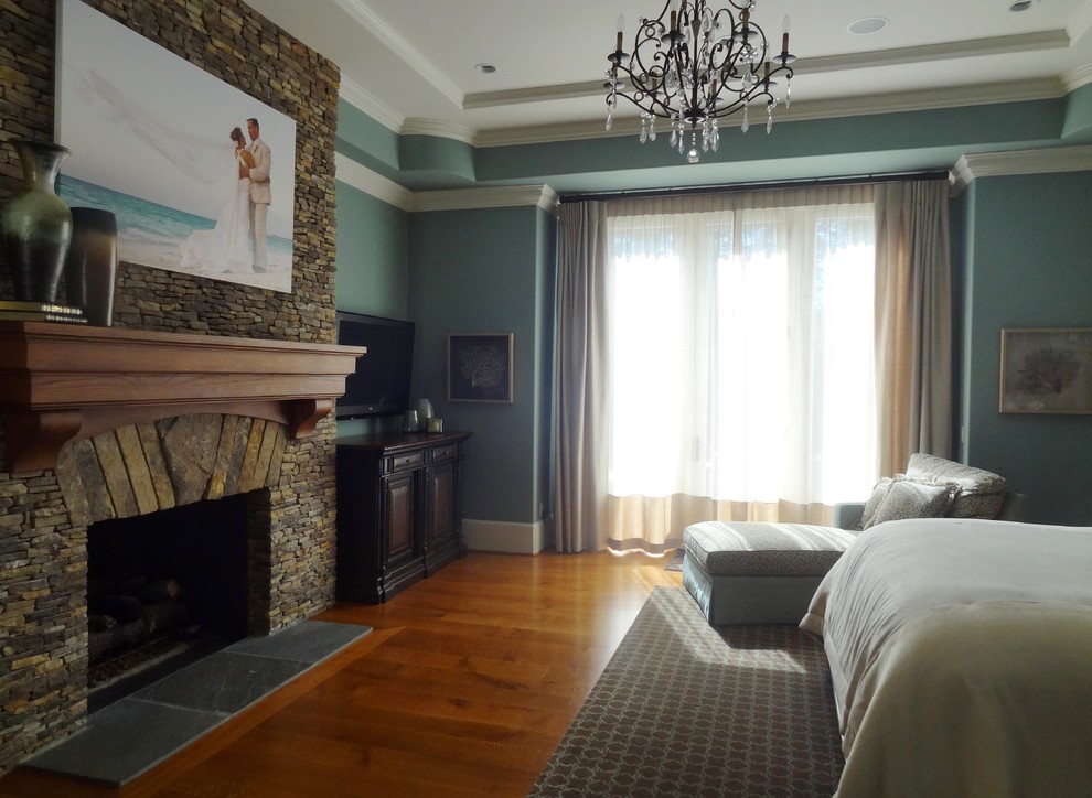 Imagen de dormitorio principal tradicional grande con paredes grises, suelo de madera en tonos medios, todas las chimeneas y marco de chimenea de piedra