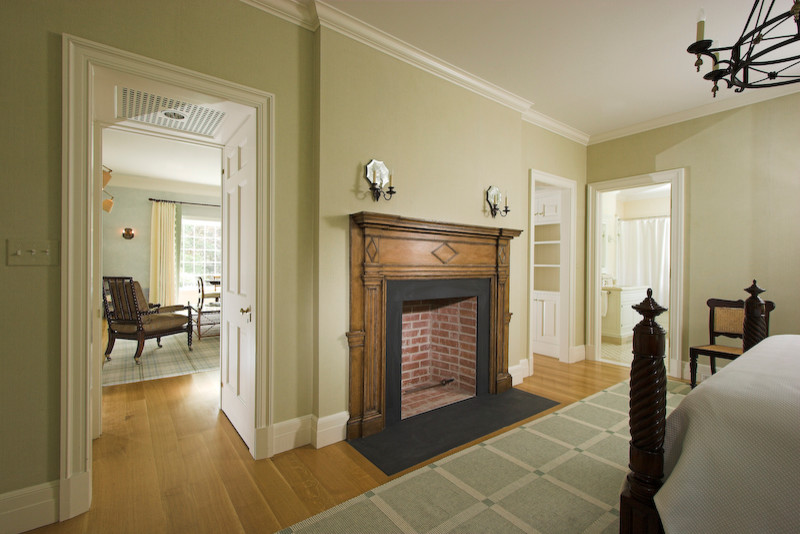 Modelo de habitación de invitados tradicional grande con paredes beige, suelo de madera en tonos medios, todas las chimeneas y marco de chimenea de madera