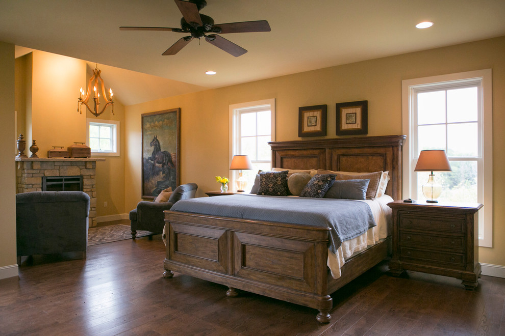 Example of a mid-sized farmhouse master medium tone wood floor bedroom design in Other with yellow walls, a ribbon fireplace and a stone fireplace