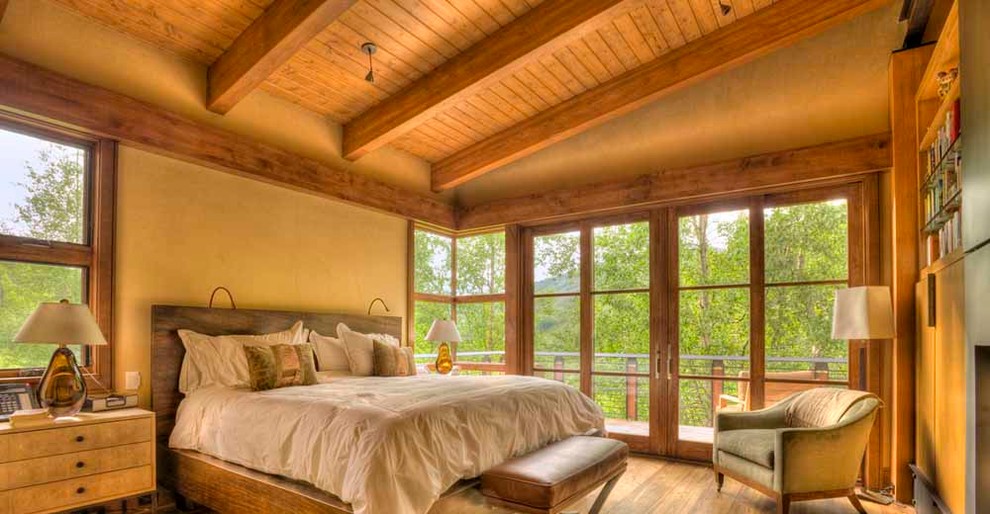 Exemple d'une grande chambre parentale moderne avec un mur beige, un sol en bois brun et une cheminée standard.