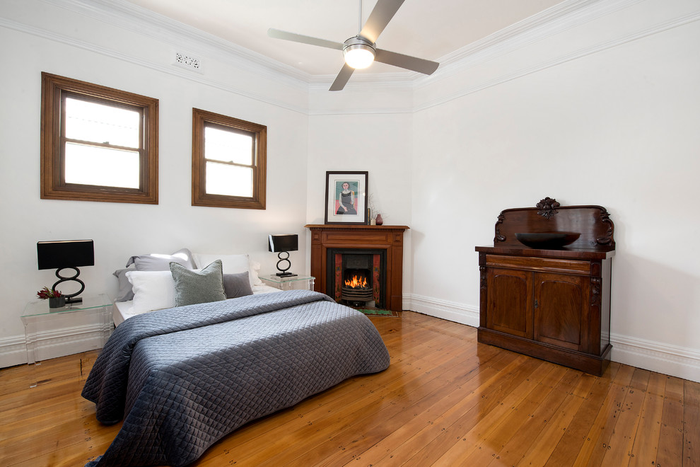 Modelo de habitación de invitados minimalista con paredes blancas, suelo de madera en tonos medios, chimenea de esquina y marco de chimenea de madera