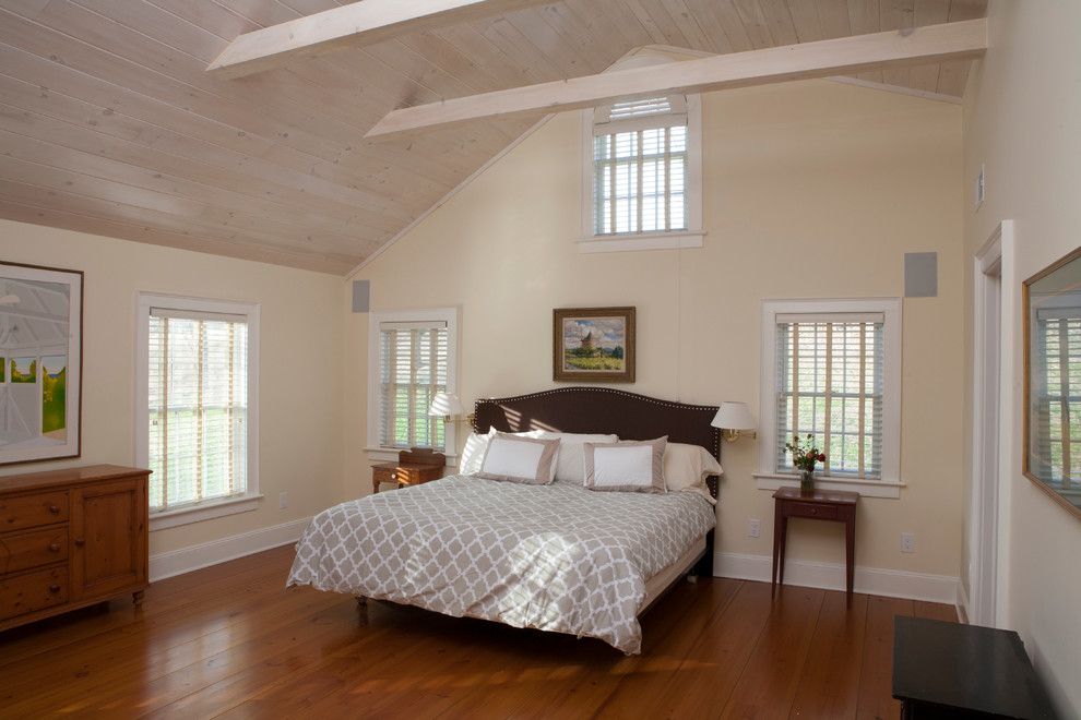 Modelo de dormitorio principal campestre grande con paredes beige, suelo de madera en tonos medios, todas las chimeneas y marco de chimenea de madera