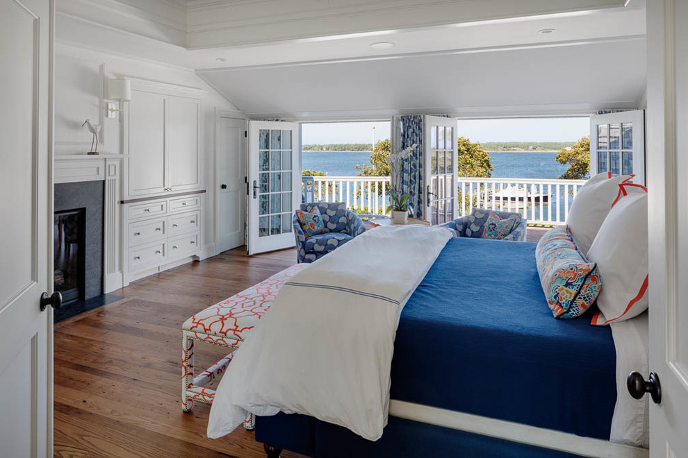 Imagen de dormitorio principal marinero grande con paredes blancas, suelo de madera en tonos medios, todas las chimeneas y marco de chimenea de baldosas y/o azulejos