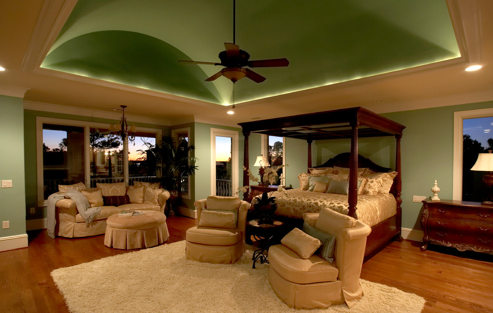 Ejemplo de dormitorio principal clásico con paredes verdes, suelo de madera en tonos medios, todas las chimeneas y marco de chimenea de piedra