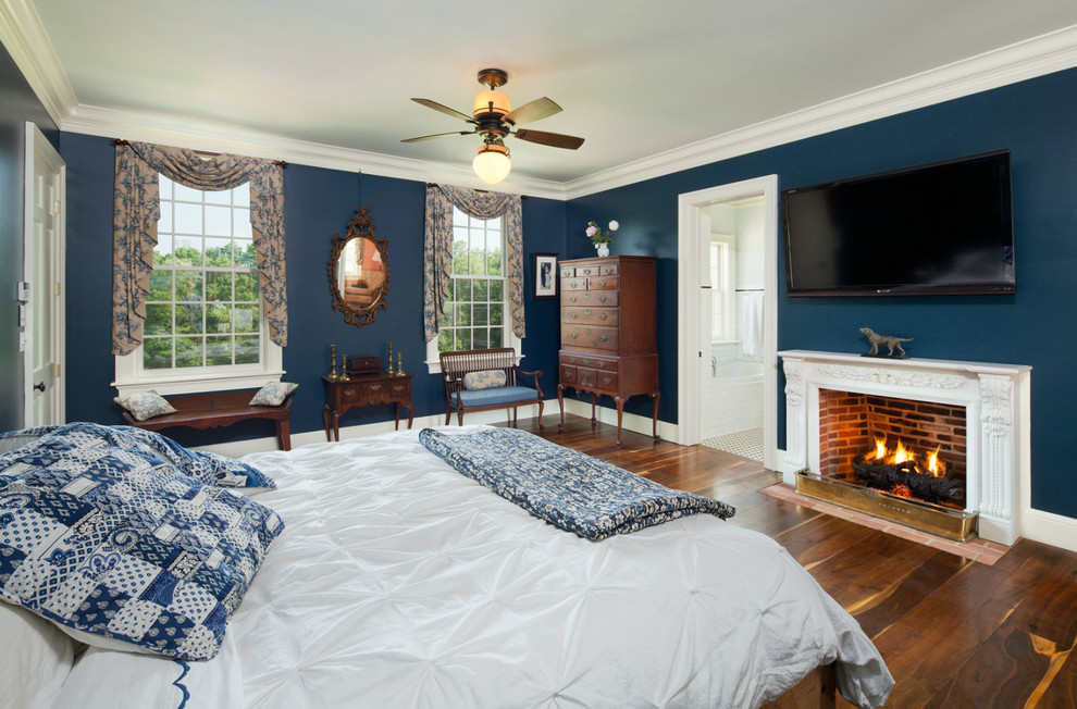 Modelo de dormitorio principal tradicional grande con paredes azules, suelo de madera en tonos medios, todas las chimeneas y marco de chimenea de madera