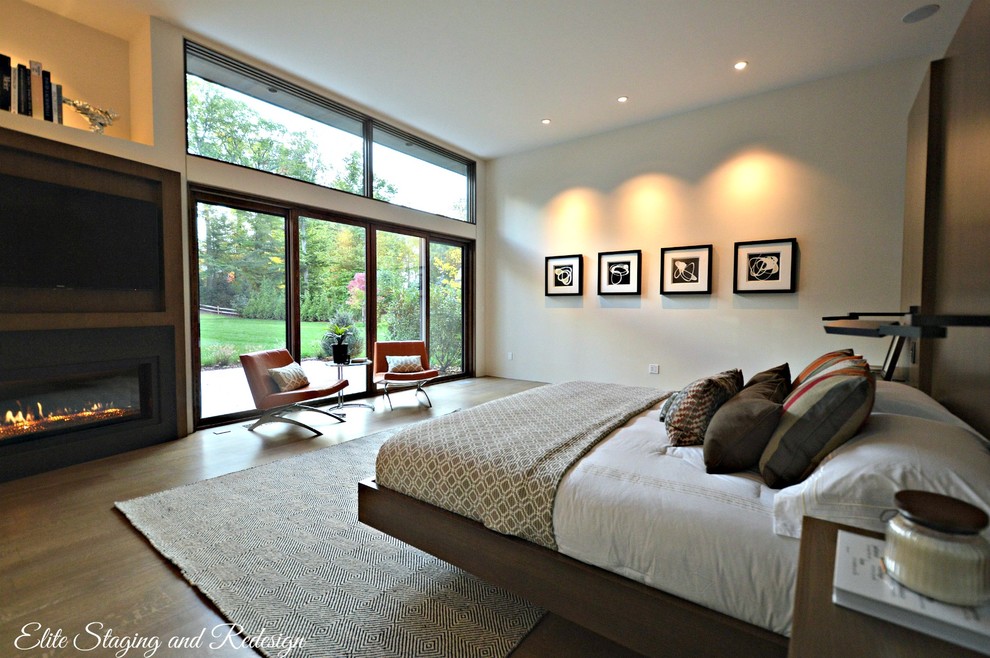 Imagen de dormitorio principal actual grande con paredes blancas, suelo de madera en tonos medios, todas las chimeneas y marco de chimenea de metal