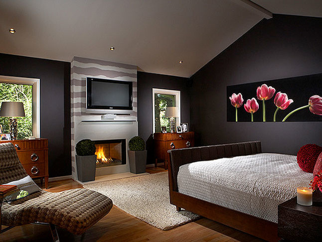 На фото: хозяйская спальня среднего размера с черными стенами, светлым паркетным полом, стандартным камином и фасадом камина из штукатурки с