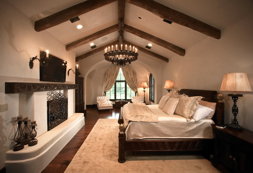 Großes Mediterranes Hauptschlafzimmer mit weißer Wandfarbe, dunklem Holzboden, Kamin, verputzter Kaminumrandung und braunem Boden in Houston