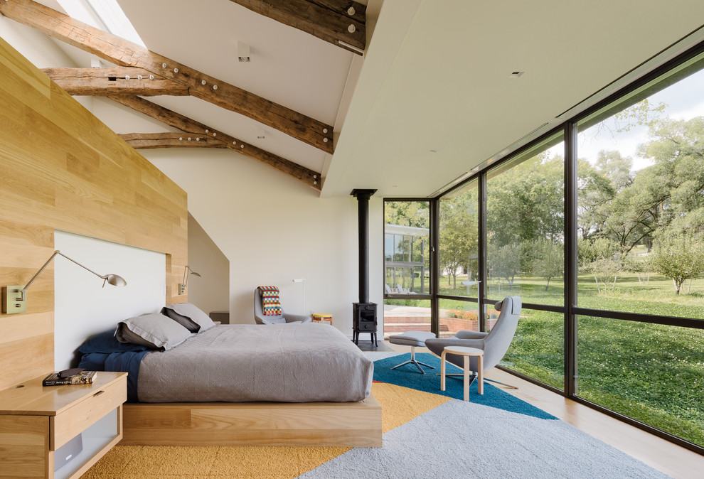 Idée de décoration pour une chambre champêtre avec un mur blanc, un sol en bois brun, un poêle à bois et un sol marron.