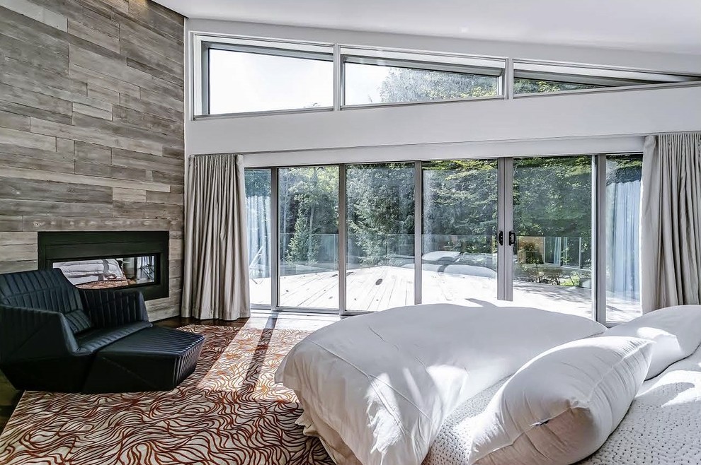 Large trendy master medium tone wood floor and brown floor bedroom photo in Toronto with white walls, a wood fireplace surround and a ribbon fireplace