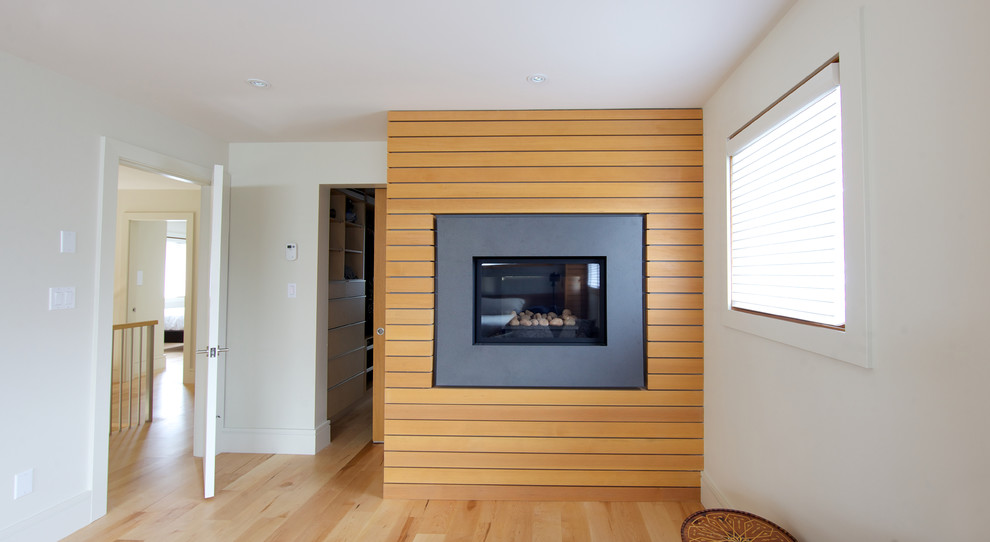 バンクーバーにある広いコンテンポラリースタイルのおしゃれな主寝室 (白い壁、淡色無垢フローリング、標準型暖炉、木材の暖炉まわり) のインテリア