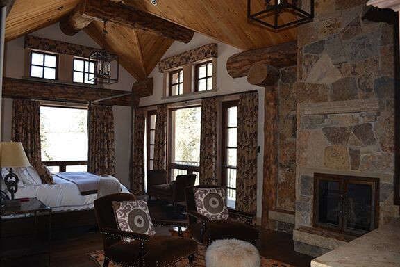 Cette image montre une grande chambre parentale chalet avec un mur blanc, parquet foncé, une cheminée standard et un manteau de cheminée en pierre.