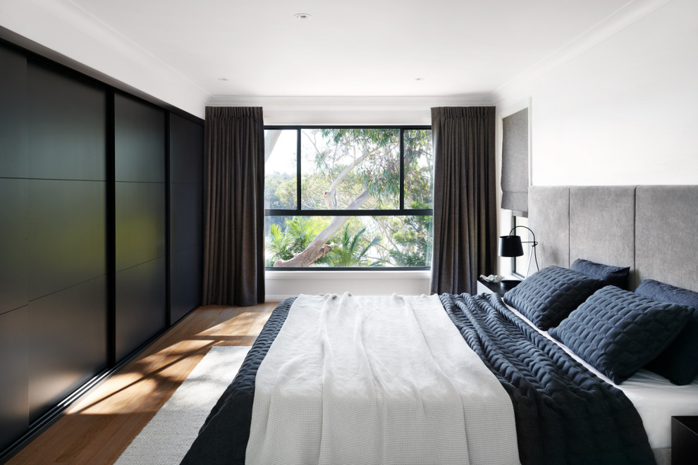 Large trendy medium tone wood floor and brown floor bedroom photo in Sydney with white walls and no fireplace