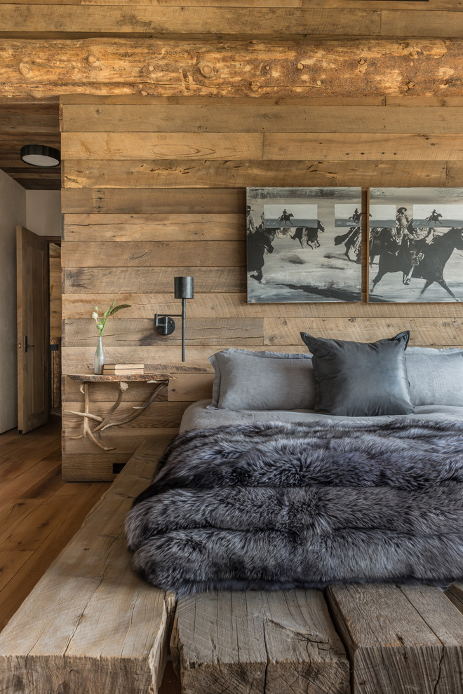 Large rustic guest and grey and brown bedroom in Other with beige walls, medium hardwood flooring, a standard fireplace, a stone fireplace surround and brown floors.