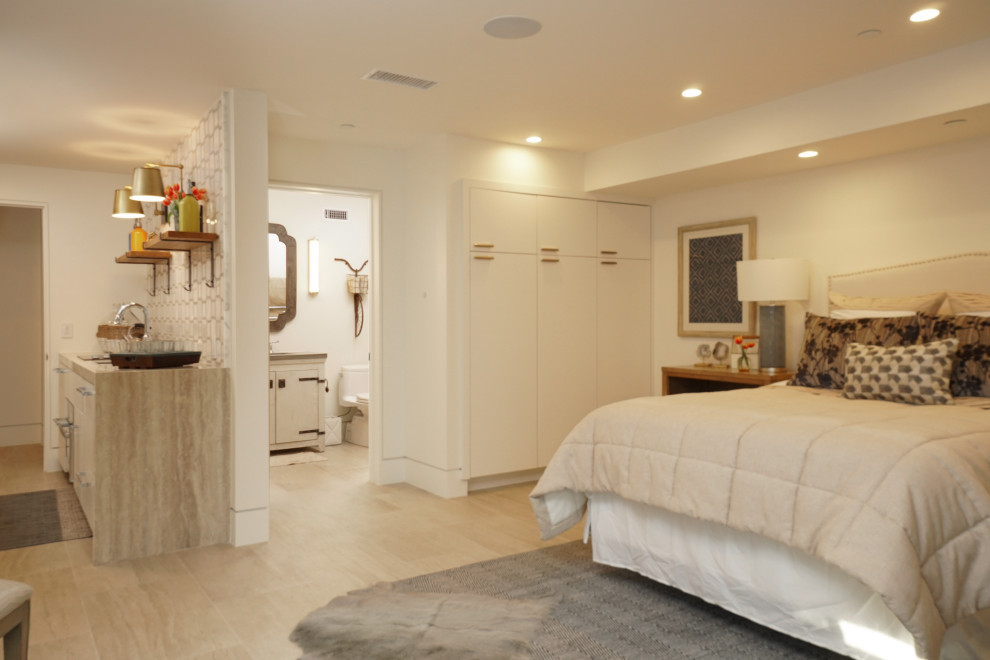 Großes Hauptschlafzimmer mit weißer Wandfarbe, hellem Holzboden, Kamin, verputzter Kaminumrandung und beigem Boden in Orange County