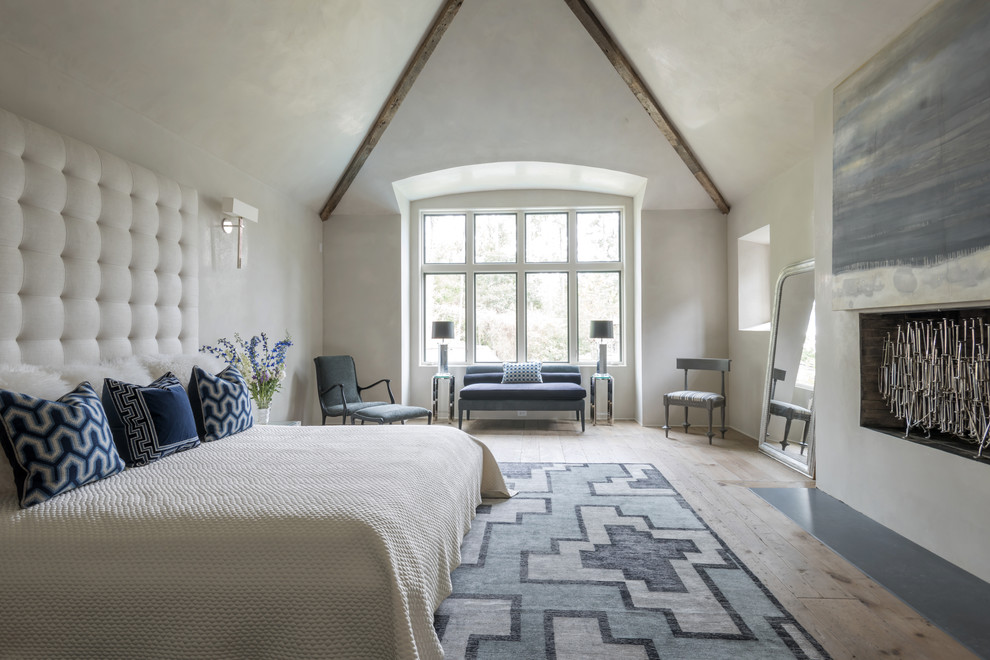 Imagen de dormitorio principal campestre grande con paredes blancas, suelo de madera clara, chimenea lineal, suelo beige y techo inclinado