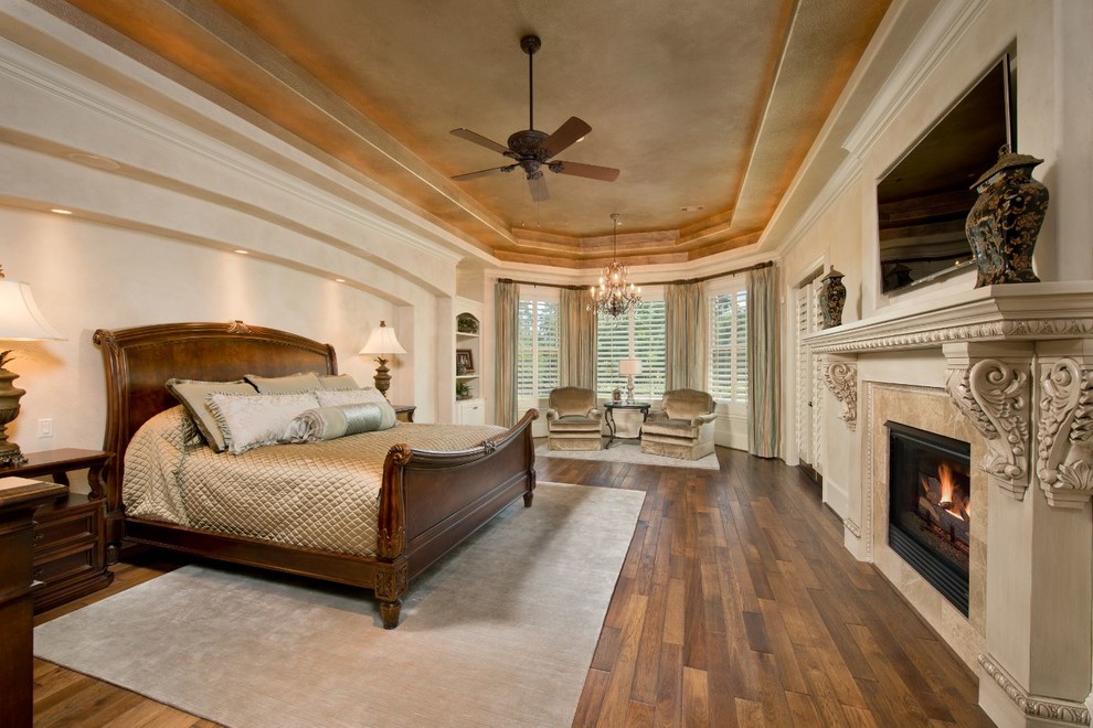 Стильный дизайн: большая хозяйская спальня в классическом стиле с бежевыми стенами, паркетным полом среднего тона, стандартным камином, фасадом камина из штукатурки и коричневым полом - последний тренд