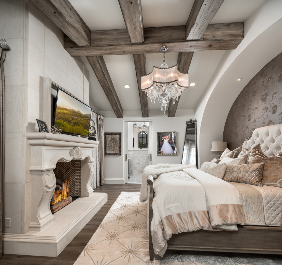 Geräumiges Shabby-Look Hauptschlafzimmer mit weißer Wandfarbe, dunklem Holzboden, Tunnelkamin, Kaminumrandung aus Stein, braunem Boden und freigelegten Dachbalken in Phoenix