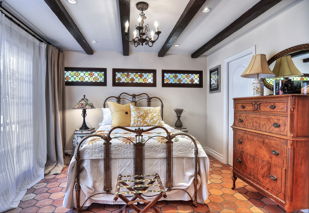 Mittelgroßes Mediterranes Gästezimmer mit weißer Wandfarbe, Terrakottaboden, Kamin, Kaminumrandung aus Stein und braunem Boden in Orange County