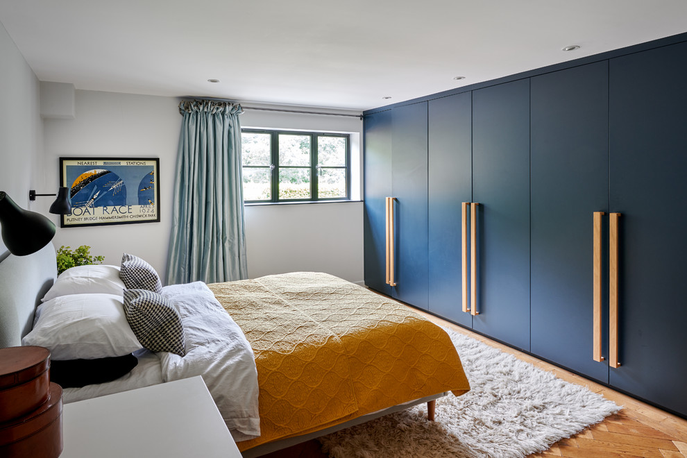 ハンプシャーにある中くらいなコンテンポラリースタイルのおしゃれな主寝室 (白い壁、無垢フローリング、暖炉なし、茶色い床、青いカーテン、グレーとブラウン) のレイアウト