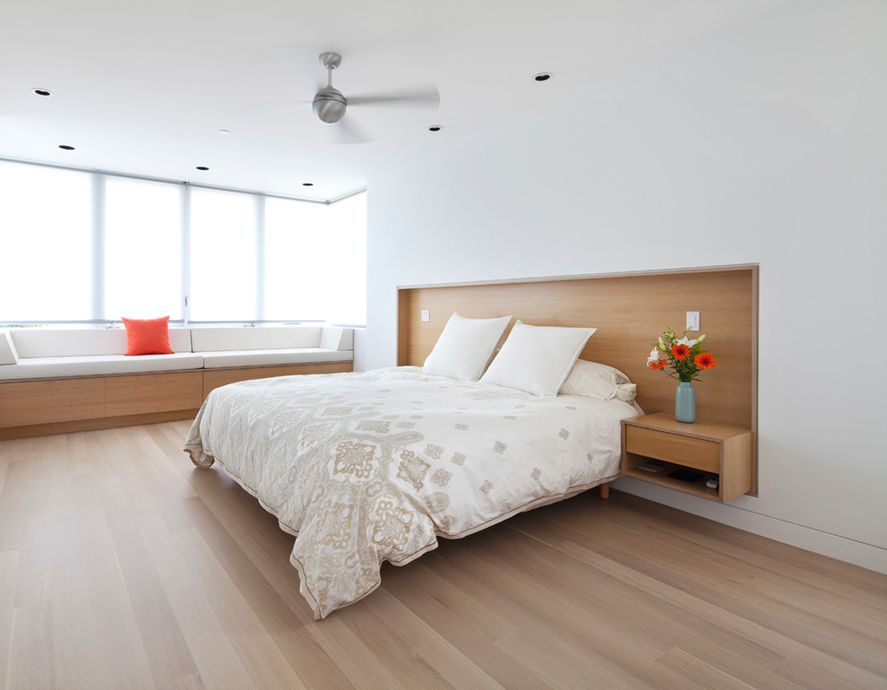 Modelo de dormitorio principal contemporáneo de tamaño medio sin chimenea con paredes blancas, suelo de madera clara y suelo marrón
