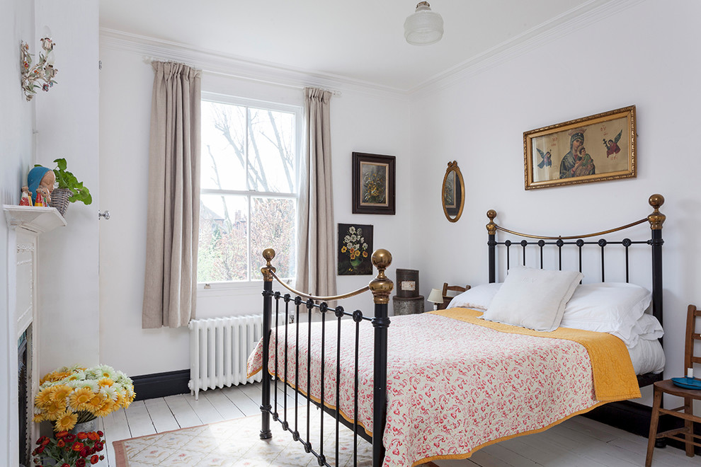 Klassisk inredning av ett mellanstort sovrum, med vita väggar, målat trägolv, vitt golv och en standard öppen spis