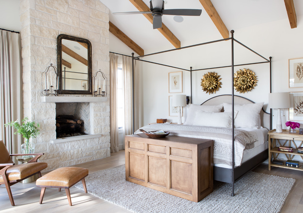 Imagen de dormitorio principal de estilo de casa de campo con paredes blancas, suelo de madera clara y todas las chimeneas