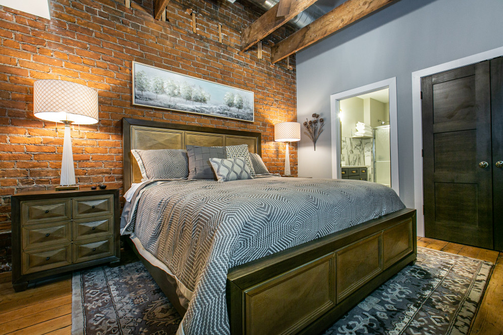 Immagine di una camera da letto industriale con pareti grigie, pavimento in legno massello medio, pavimento marrone, travi a vista e pareti in mattoni