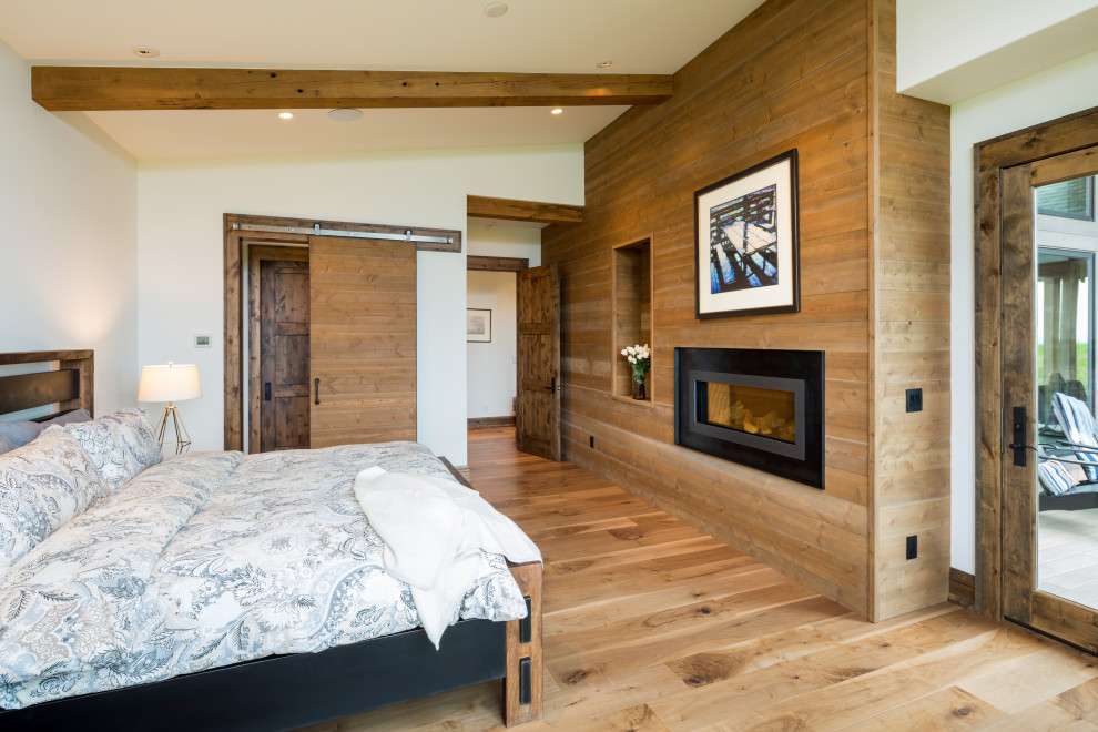 Ejemplo de dormitorio principal rural de tamaño medio con paredes blancas, suelo de madera en tonos medios, todas las chimeneas, marco de chimenea de metal y suelo marrón