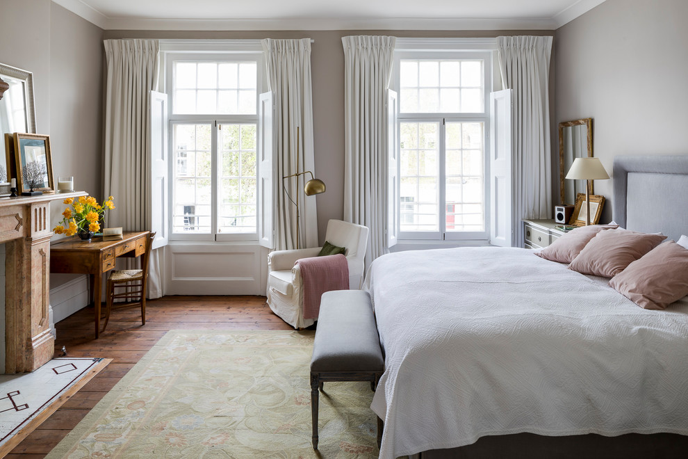 Klassisches Hauptschlafzimmer mit grauer Wandfarbe, Kaminumrandung aus Stein, braunem Holzboden, Kamin und braunem Boden in London