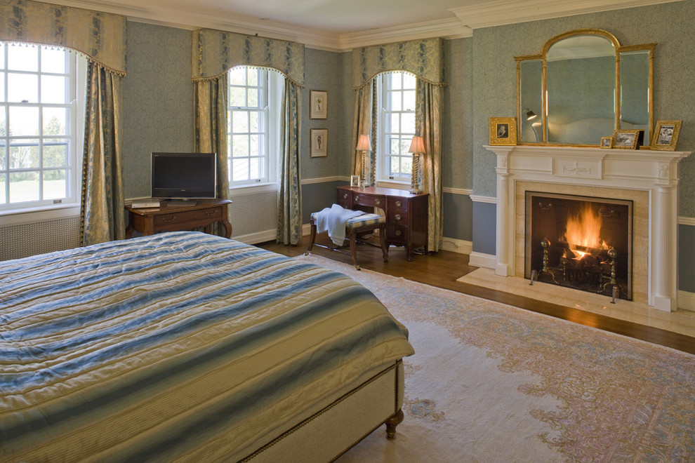 Exempel på ett klassiskt sovrum, med blå väggar, mellanmörkt trägolv, en standard öppen spis och en spiselkrans i sten