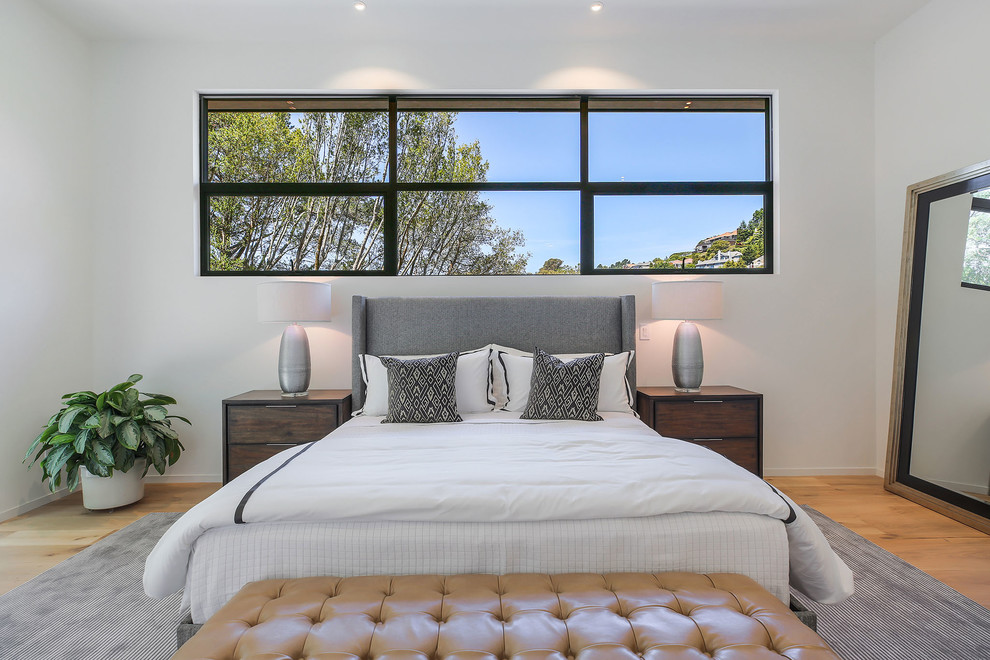 Modelo de dormitorio contemporáneo con paredes blancas, suelo de madera en tonos medios y suelo marrón