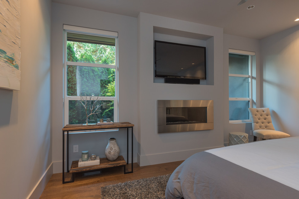 Ejemplo de habitación de invitados actual de tamaño medio sin chimenea con paredes grises, suelo de madera en tonos medios y marco de chimenea de metal